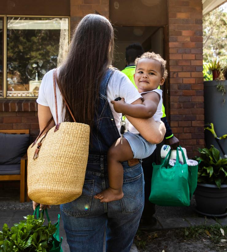 Madre sosteniendo a su hija caminando hacia la puerta principal.